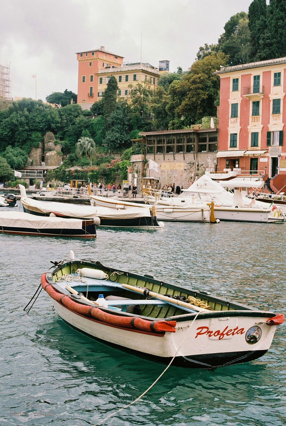 A small wooden boat named Profeta moored in a harbour, pastel buildings on the hillside behind.