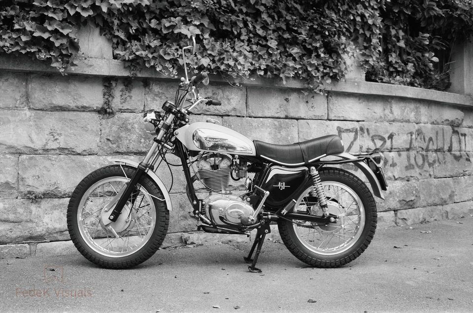 Black and white: a cafe racer motorcycle parked against a stone wall under ivy.