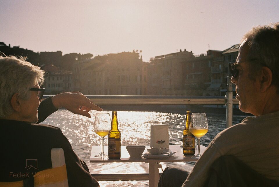 Two people at an outdoor table, backlit by low sun, beer glasses between them and their faces lost to the flare.