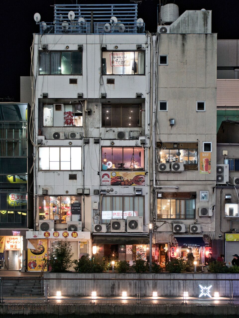 A tall city building at night, every floor a lit window of restaurants stacked one above another.