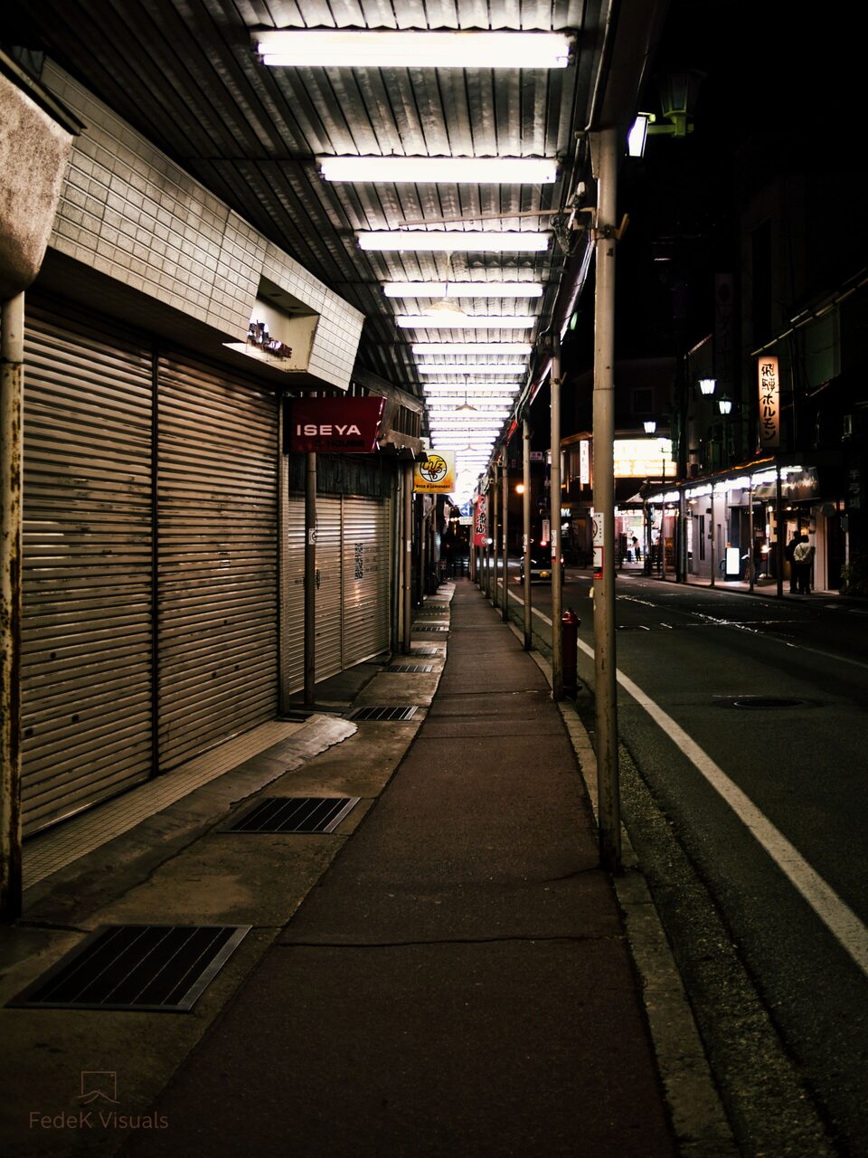 A long covered shopping arcade with shuttered fronts receding to a bright point in the distance.